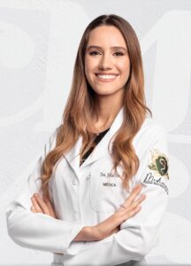 Fotografia de mulher branca, loira, cabelos longos, braços cruzados, de jaleco